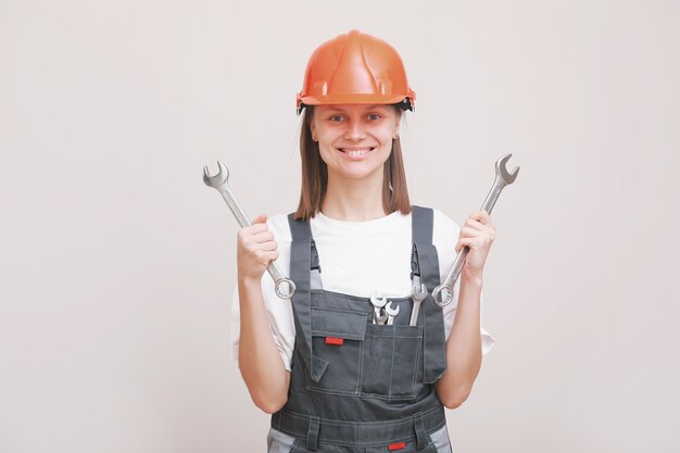 Junge schöne Mädchen Ingenieur in einer grauen Uniform und Schutzhelm lächelt mit Werkzeugen, Schraubenschlüssel in ihren Händen.