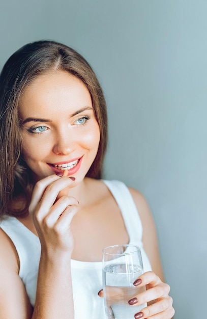 Junge schöne Mädchen oder Frauen nehmen eine Pille oder Tablette mit einem Glas Wasser in der Nähe des Fensters