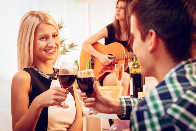 Junge schöne Mädchen und ihr Freund stoßen mit Rotwein auf der Hausparty an. Selektiver Fokus.