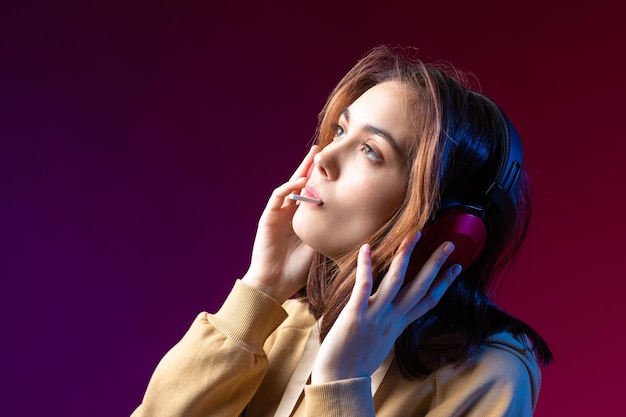 Junge schöne modische Hipster-Mädchen in einem Hoodie, die Musik in roten Kopfhörern in einem roten dramatischen Studiohintergrund hört