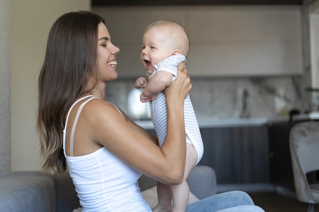 Junge schöne Mutter sitzt auf der Couch. Hält ein neugeborenes Baby in ihren Armen. spielen Sie mit Ihrem Kind. Glückliches Familienkonzept