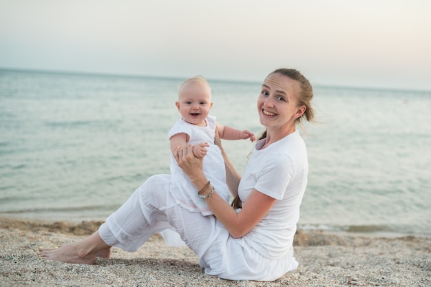 Junge schöne Mutter und Baby sitzen am Sandstrand