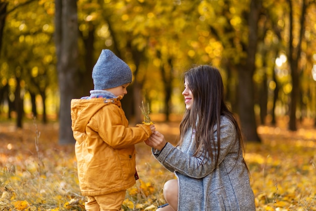 Junge schöne Mutter verbringt Zeit mit ihrem geliebten kleinen Sohn im Herbstpark spazieren.