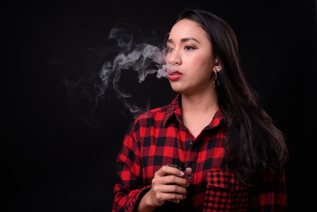 junge schöne philippinische Frau, die gegen schwarze Wand vaping