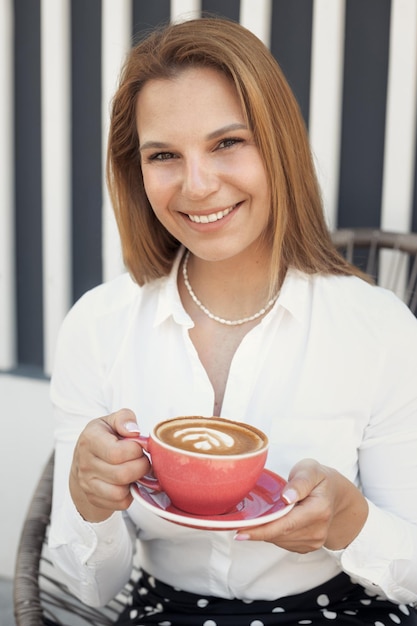 Junge schöne rothaarige Frau in weißem Hemd, die sich nach der Arbeit in einem Straßencafé entspannt und Kaffee trinkt