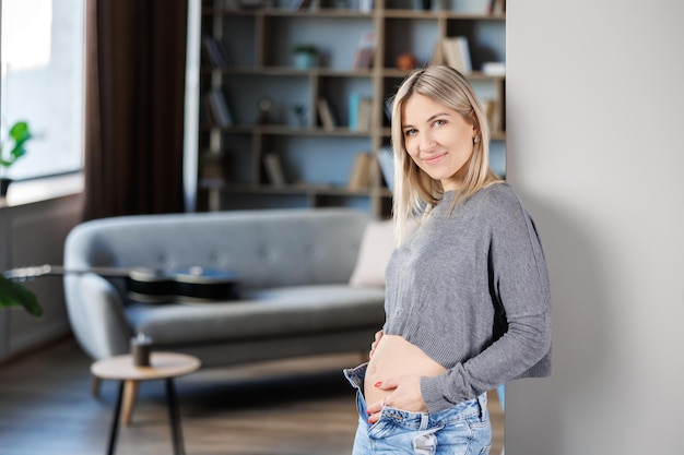 Junge schöne schwangere Frau, die zu Hause in der Nähe der Wand steht