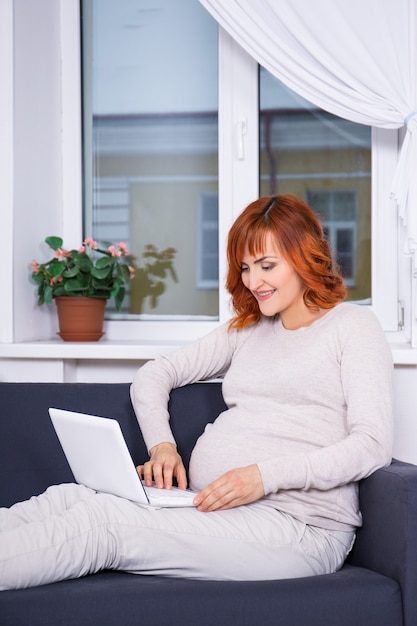 Junge schöne schwangere Frau mit Laptop im Wohnzimmer