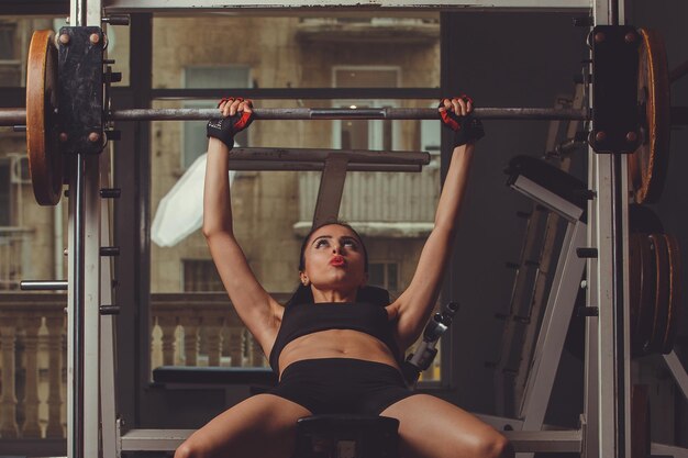 Junge schöne sexy blonde Sportlerin trainiert im Fitnessstudio in schöner Sportbekleidung auf dunklem Hintergrund