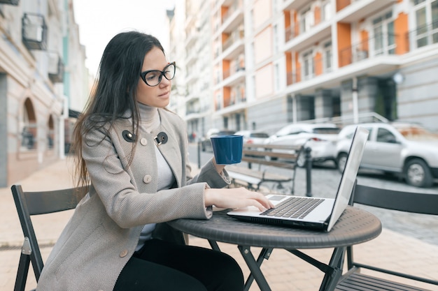 Junge schöne Studentin in einem Café im Freien mit Laptop