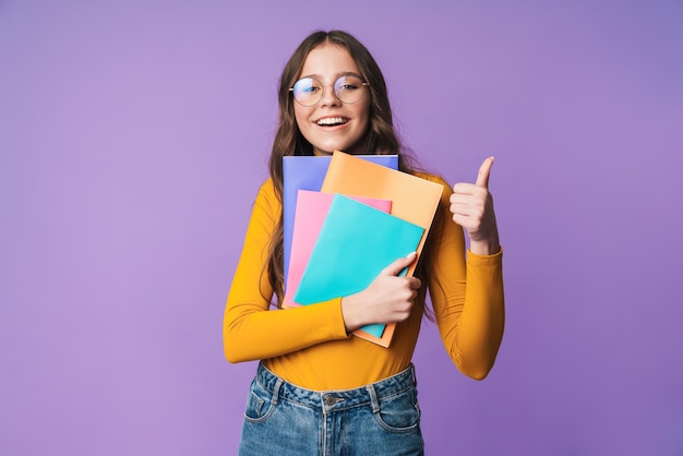 junge schöne Studentin mit Brille lächelt und hält Schulhefte isoliert