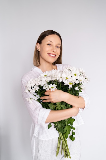 Junge schöne süße süße lächelnde Frau mit einem Strauß weißer frischer Blumen auf weißem Wandhintergrund