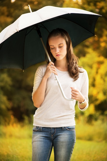 Junge Schönheit, die im regnerischen Herbstpark mit Regenschirm steht.