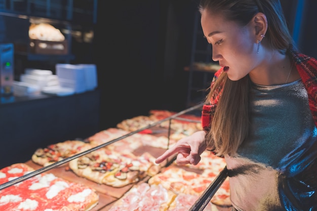 Junge Schönheit im karierten Hemd, das eine Pizzascheibe kauft