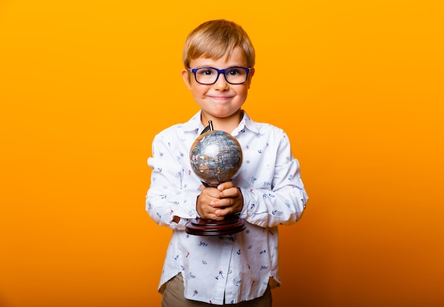 Junge Schuljunge 7 Jahre alter Schuljunge in Gläsern mit einem Globus in den Händen lächelnd auf einem gelben Hintergrund