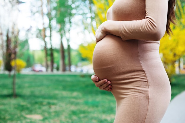 Junge schwangere Frau, die draußen im Stadtpark steht und ihren Bauch hält Mutterschaft Schwangerschaft Menschen und Erwartungskonzept