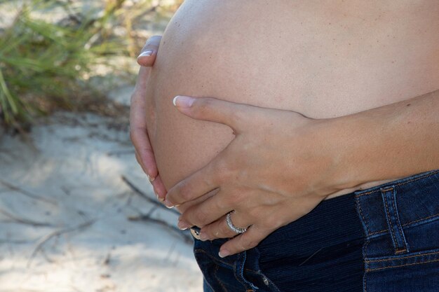 Foto junge schwangere frau, die ihren nackten bauch mit den händen im freien umarmt