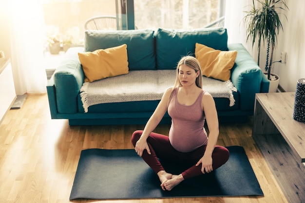 Junge schwangere Frau, die morgens zu Hause Yoga ausübt. Sie macht Dehnübungen.