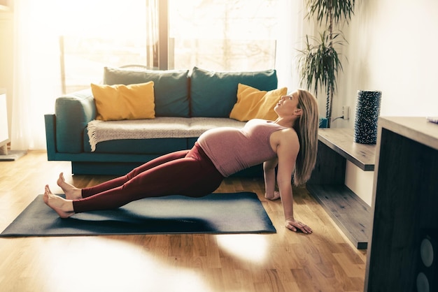 Junge schwangere Frau, die morgens zu Hause Yoga ausübt. Sie macht Dehnübungen.