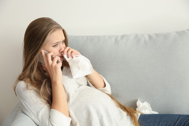 Junge schwangere Frau, die per Telefon spricht und wegen Stimmungsänderung weint