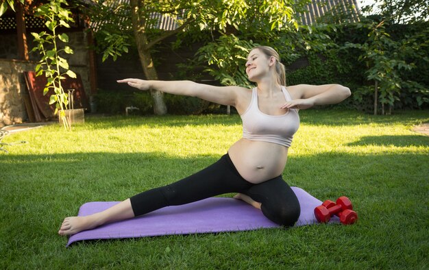 Junge schwangere Frau, die sich am sonnigen Tag im Park ausdehnt