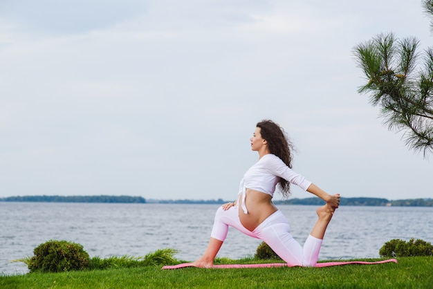 Junge schwangere Frau, die Yoga im Freien tut