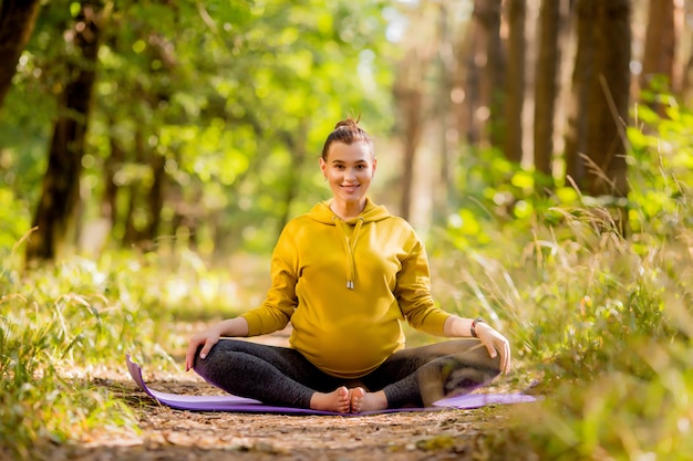 junge schwangere Frau, die Yoga im Sommer im Wald tut