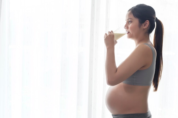 Junge schwangere Frau, die zu Hause Milch trinkt, Gesundheitsfürsorge und Schwangerschaftspflege