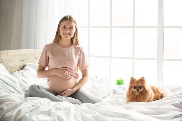 Junge schwangere Frau erwartet ein Baby, das sich zu Hause mit Hund auf dem Bett entspannt