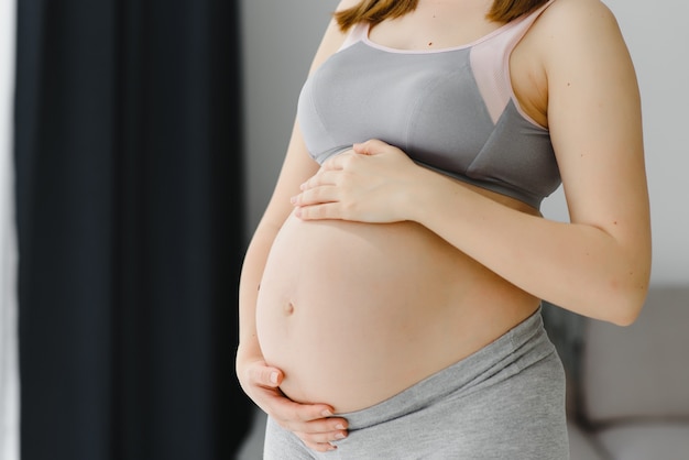 Junge schwangere Frau hält ihre Hände auf ihrem geschwollenen Bauch. Liebe Konzept. Horizontal mit Textfreiraum