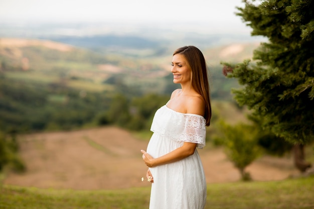 Junge schwangere Frau im weißen Kleid am Sommerfeld