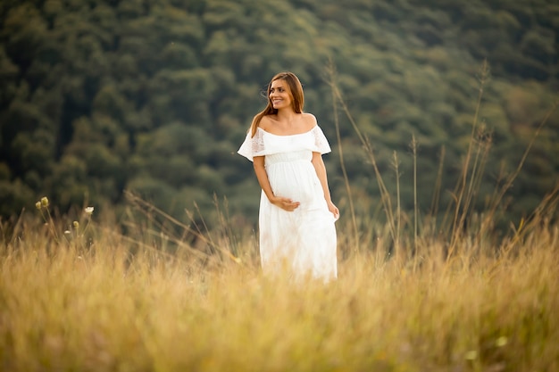 Junge schwangere Frau im weißen Kleid am Sommerfeld