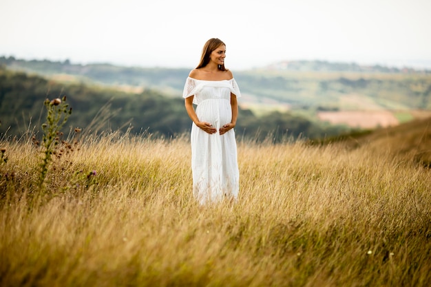 Junge schwangere Frau im weißen Kleid am Sommerfeld