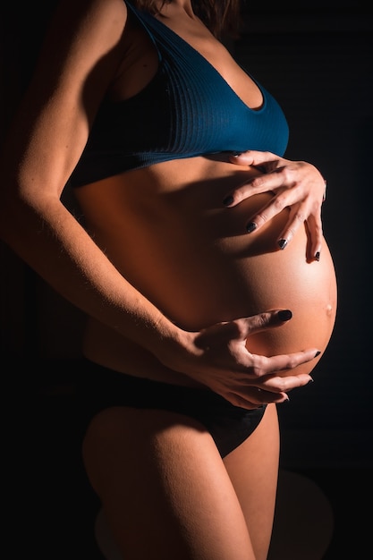 Junge schwangere Frau kurz vor der Geburt. Mit den Händen auf dem Bauch. In einigen Studiofotos