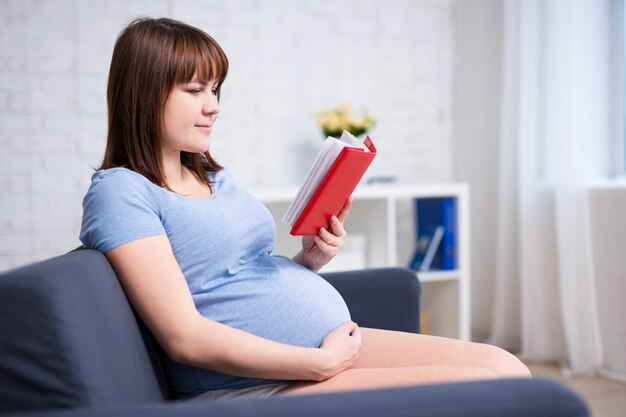 Junge schwangere Frau liest Buch im modernen Wohnzimmer