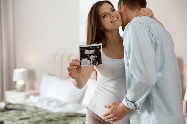 Junge schwangere Frau mit ihrem Mann im Schlafzimmer konzentriert sich auf das Ultraschallbild des Babys