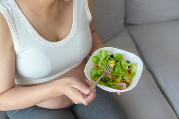 Junge schwangere Frau mit Salat zu Hause Gesundheitsversorgung und Schwangerschaftspflege