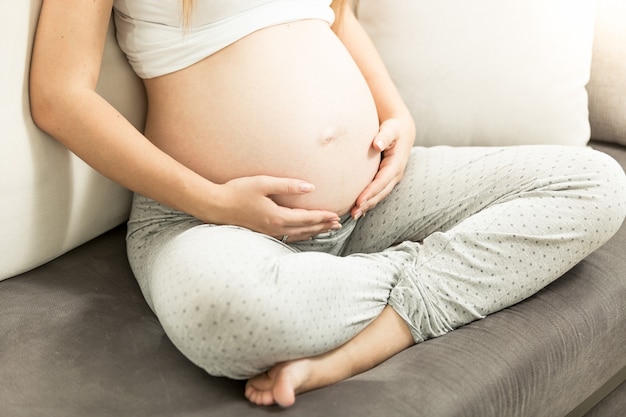 Junge schwangere Frau sitzt auf der Couch und hält den Bauch