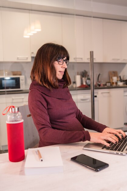 Junge schwangere Frau Telearbeit mit dem Computer von zu Hause wegen der Schwierigkeiten der Arbeit