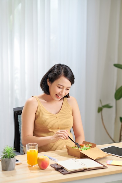 Junge schwangere Frau unter Verwendung der digitalen Tablette, die frischen Salat und Früchte auf Tisch isst