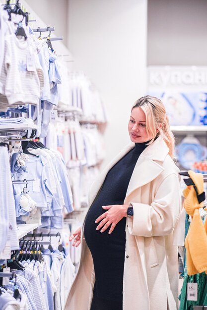 Junge schwangere Frau wählt Neugeborenenkleidung in einem Babyshop aus