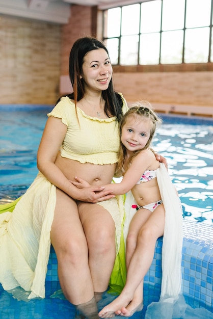 Junge schwangere Mutter mit einem Mädchen am Hallenbad Mutter und Tochter bereiten sich auf das Schwimmen vor