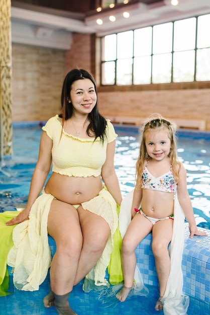 Junge schwangere Mutter mit einem Mädchen am Hallenbad Mutter und Tochter bereiten sich auf das Schwimmen vor