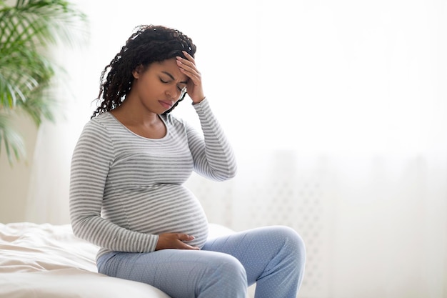 Junge schwangere schwarze Frau, die zu Hause unter Kopfschmerzen oder Migräne leidet