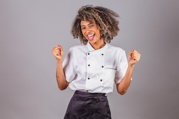 Junge schwarze Brasilianerin Köchin Masterchef trägt Restaurantuniform und feiert extrem glücklich