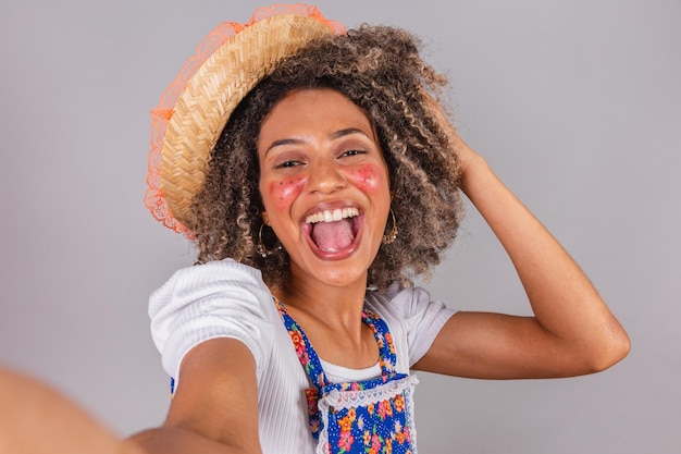 Junge schwarze Brasilianerin mit Landkleidung, gekleidet für Festa Junina Saint John's Festival Pose für Selfie mit Smartphone