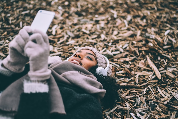 Junge schwarze Frau am Handy, der auf Frieden des Holzes nahe dem königlichen Palast in Madrid während des Winters liegt