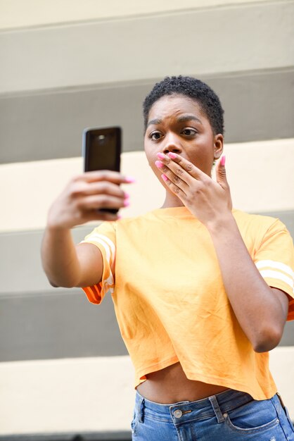 Junge schwarze Frau, die draußen selfie Fotos mit lustigem Ausdruck macht.