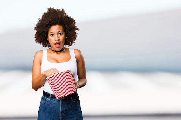 junge schwarze Frau, die einen Popcorneimer anhält