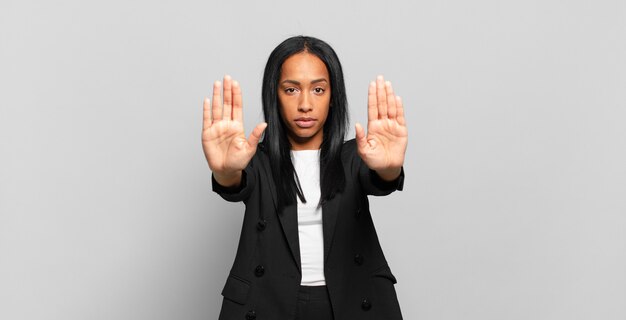 Junge schwarze Frau, die ernst, unglücklich, wütend und unzufrieden aussieht und den Eintritt verbietet oder mit beiden offenen Handflächen aufhört. Geschäftskonzept