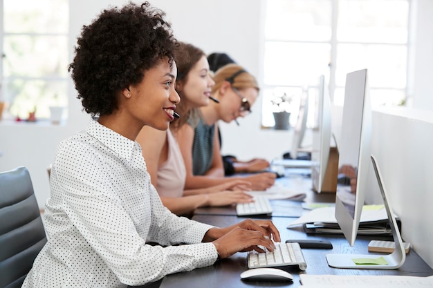 Junge schwarze Frau, die im Büro mit Headset am Computer arbeitet